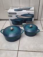 Box and both teal enameled cast iron Dutch ovens with lids displayed