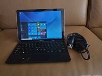 Front view powered on showing Windows 10 start menu, keyboard attached, charger beside