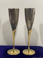 Two brass and silver-tone metal champagne flutes standing upright