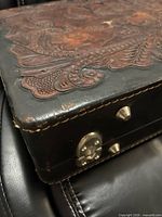Corner of briefcase showing carved leather top, metal feet, latch and edge wear