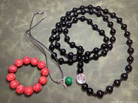 All three jewelry pieces laid out: red bracelet, green pendant necklace, black bead necklace with clear bead
