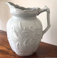 Front view of white ironstone jug showing wheat relief pattern and scalloped rim