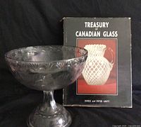 Clear pressed glass pedestal bowl alongside Canadian glass reference book
