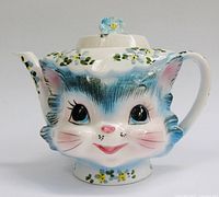 Front view of Miss Priss teapot showing cat face, spout, handle and lid with flower finial