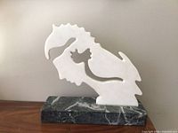 Full view of white marble abstract sculpture on green marble base against wall