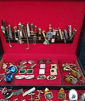 Open jewellery box showing tie clips on lid strip and cufflinks in tray