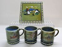 Front view of three mugs and trivet showing decoration and scale