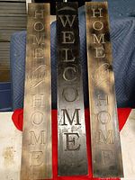 Front view of three vertical wooden porch signs showing wording and stain colors