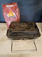 Grill closed on stand beside Cook's charcoal bag