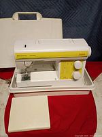 Sewing machine seated in base with hard case behind