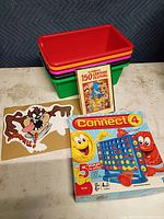 Stack of five plastic bins, Connect 4 game box, DVD set, decal sheet together