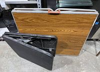 Both tables folded, black plastic and woodgrain laminate showing
