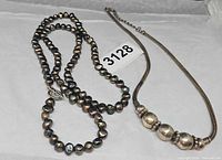 Both necklaces laid flat showing full length and design details, tag 3128 visible