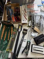 Overview of assorted packaged and loose barbecue tools, grill baskets, lighter, accessories