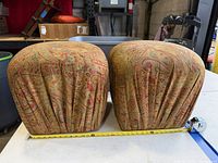 Two matching paisley footstools with tape measure showing width