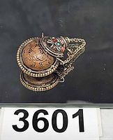 Full view of round brass snuff bottle pendant showing engraved script and filigree cap