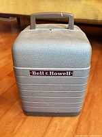 Projector packed in its hard plastic case, front view with Bell & Howell logo