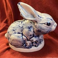 Front view of ceramic rabbit coin bank with baby bunnies and blue sponge decoration