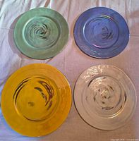 Top view of four charger plates in green, blue, yellow, white showing colors and swirl pattern