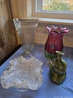 Group shot of all four items: pressed glass vase, ruffled art glass vase, spatter art glass bowl, green ceramic figurine