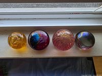 Front view of four glass paperweights lined up on windowsill