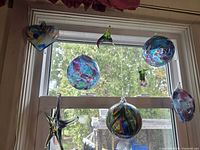 All seven glass ornaments hanging in window: heart, globes, starfish, hummingbird, teardrop
