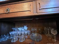 Wide view of assorted stemware, plates, salt shakers and opalescent vases on cabinet shelf