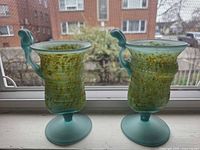 Front view of both frosted aqua and mottled yellow art glass goblets on window sill