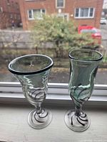 Two green-tinted cordial glasses with purple swirl accents on windowsill, side view