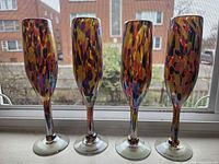 Front view of all four multi-color confetti blown glass champagne flutes on windowsill
