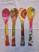 Four multicolor floral melamine serving spoons laid side by side on white cloth