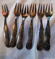 Front view of six silver-plated ornate scroll cocktail forks