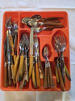 Entire flatware set in orange tray showing variety of pieces and handle colors