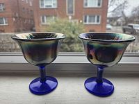 Two carnival glass goblets side by side showing cobalt stems and iridescent bowls