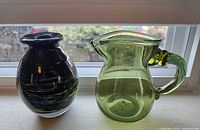 Front view of black vase and green pitcher side by side on windowsill