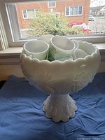 Milk glass punch bowl on pedestal with cups inside, showing overall set