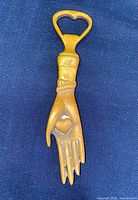 Full view of brass hand bottle opener on fabric background