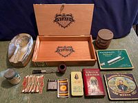 Entire lot laid out showing ashtray, pipe, lighter, cigar box, tobacco tins and paper packets