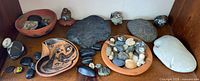 Overview of three terracotta pieces, assorted stones and painted rock figurines on shelf
