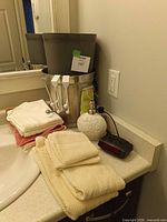 Countertop view showing towels, cloths, soap dispenser, alarm clock, stacked waste baskets and hook rack