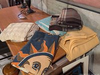 Lot overview showing all folded blankets, throw and crocheted tablecloths on table