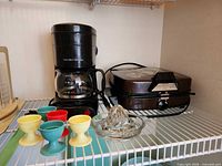 Coffee maker, waffle maker, egg cups, citrus reamer on shelf