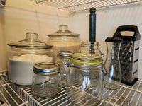 All items arranged on wire shelf: canisters, assorted jars, marble holder, grater