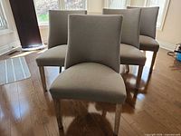 Front view of all four grey upholstered dining chairs showing seat, back, legs