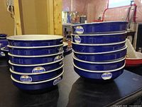 Two stacked sets of blue Emile Henry bowls with stickers visible