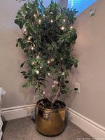 Full view of artificial ficus tree in brass planter showing string lights and lionhead handle