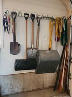 Group of shovels, ropes, driveway marker poles on wall rack