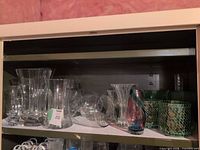 Shelf with multiple clear glass vases, green mosaic vases and multicoloured art glass piece visible