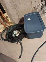 Blue Sterilite tote with lid alongside coiled hoses on basement floor