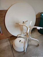 Disassembled white round tabletop, metal legs and plastic umbrella stand
